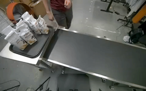 A person demonstrates handling packaged goods beside a conveyor